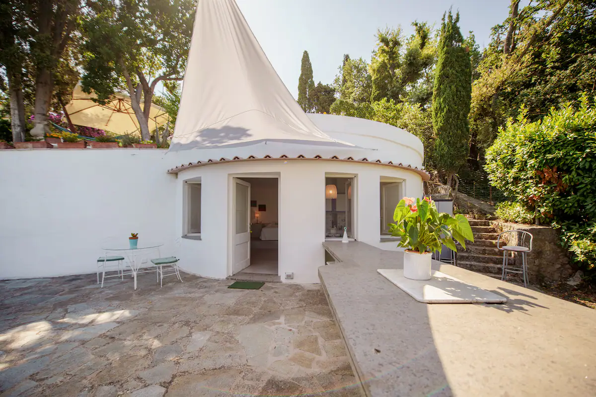 La casa rotonda bianca vista dal giardino, con la vela d'ombra e la terrazza in pietra